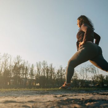 Overweight female standing and stretching with one leg behind her in runner’s pose and hands on hips